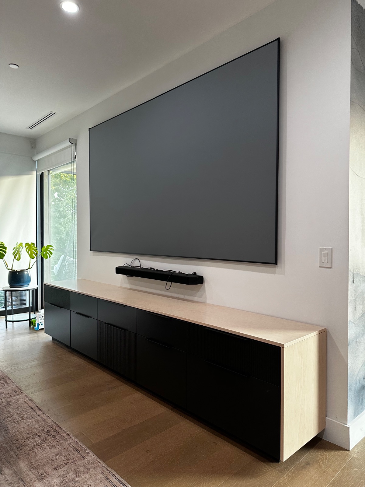A minimalist entertainment built-in with a light oak top and fluted black cabinet fronts, below a wall-mounted screen.