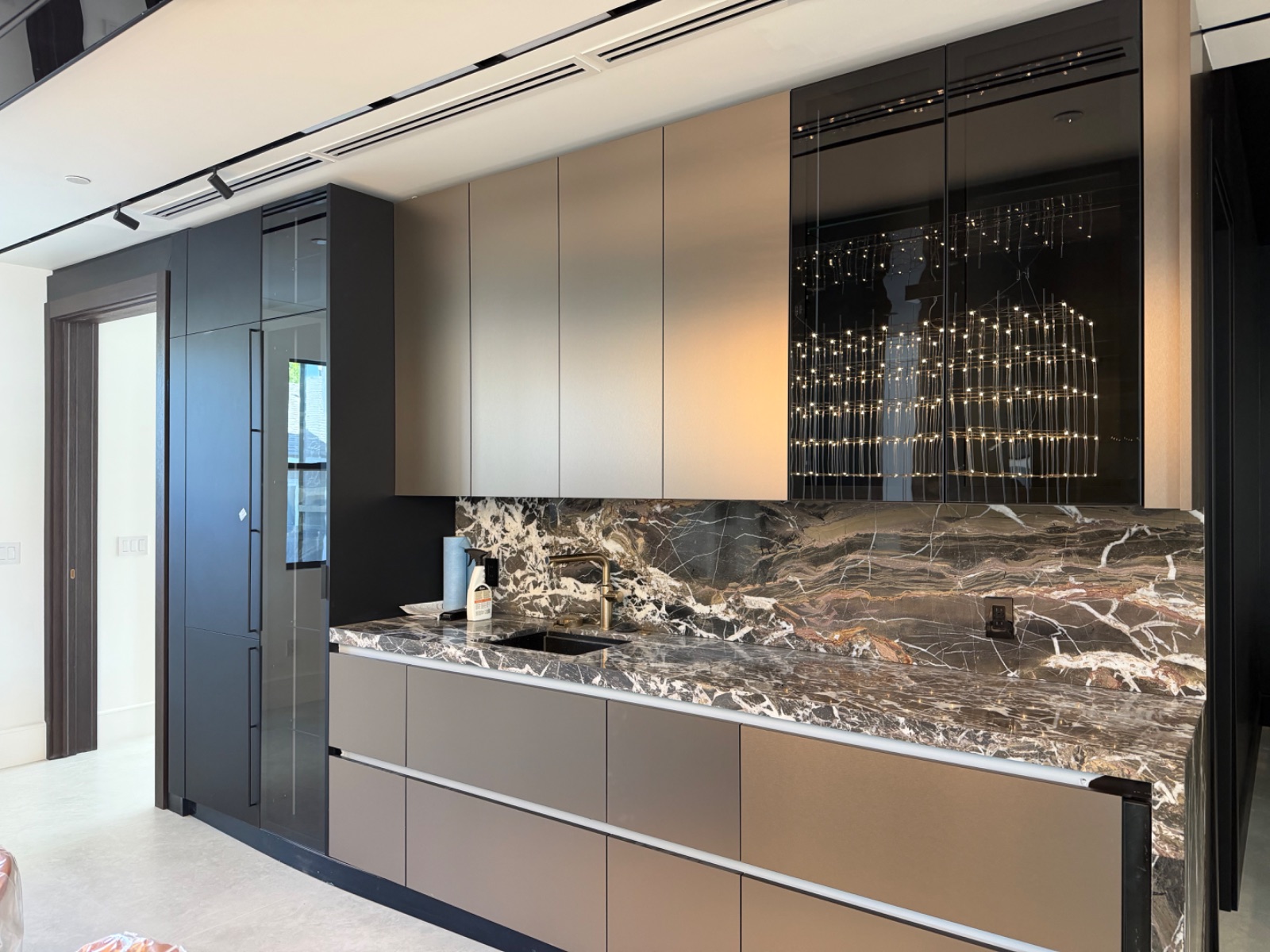 A modern home bar in black and bronze, with a dramatic black-and-white marble backsplash and pendant light cluster.