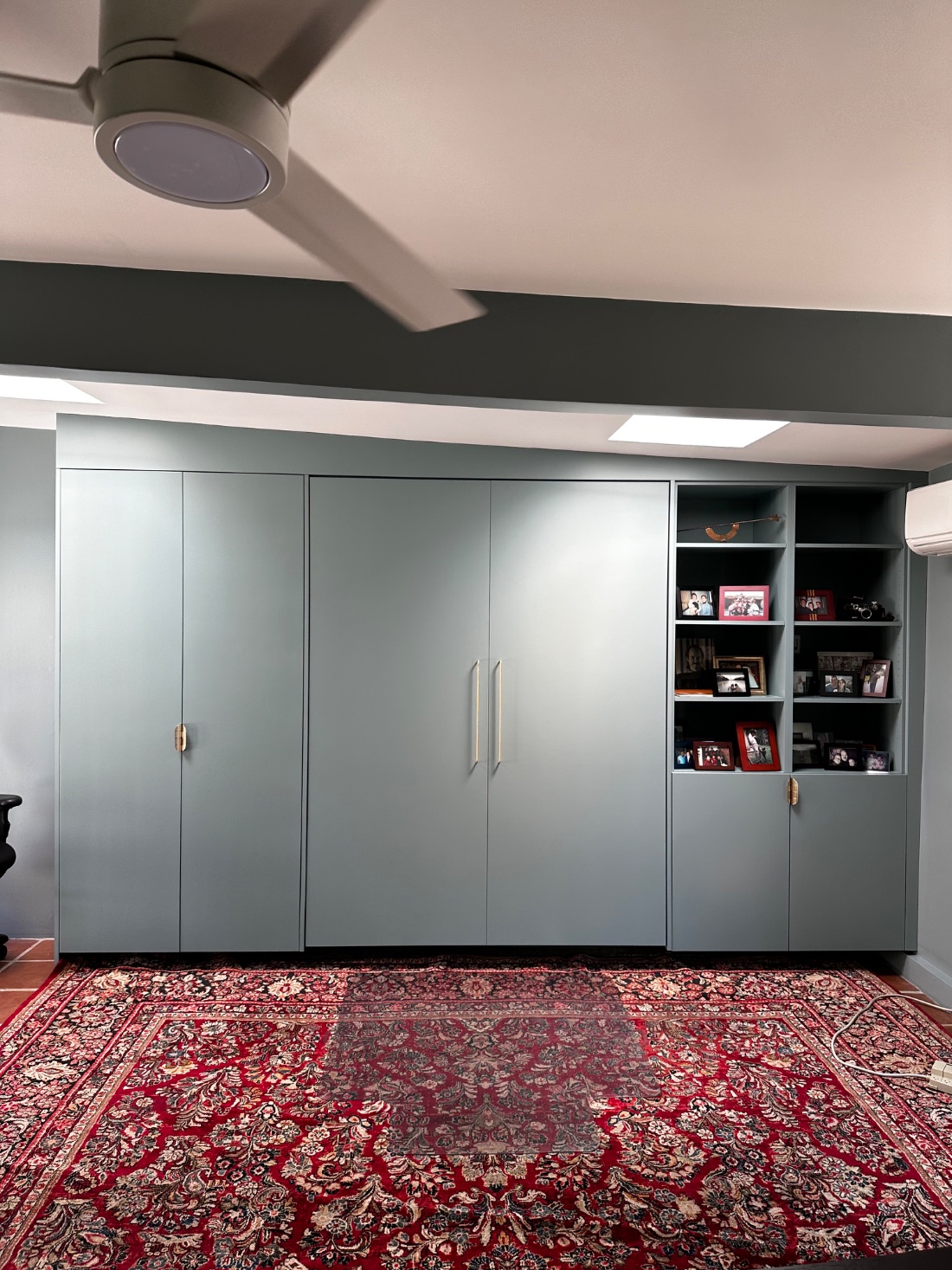 A dusty blue-green built-in wall combining a Murphy bed with a bookcase and storage cabinets.