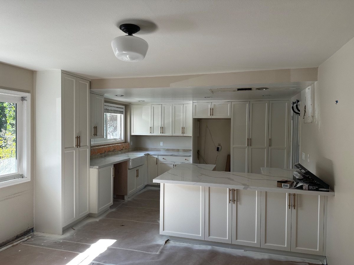 A traditional white shaker kitchen with marble counters, brass hardware, and farmhouse sink.