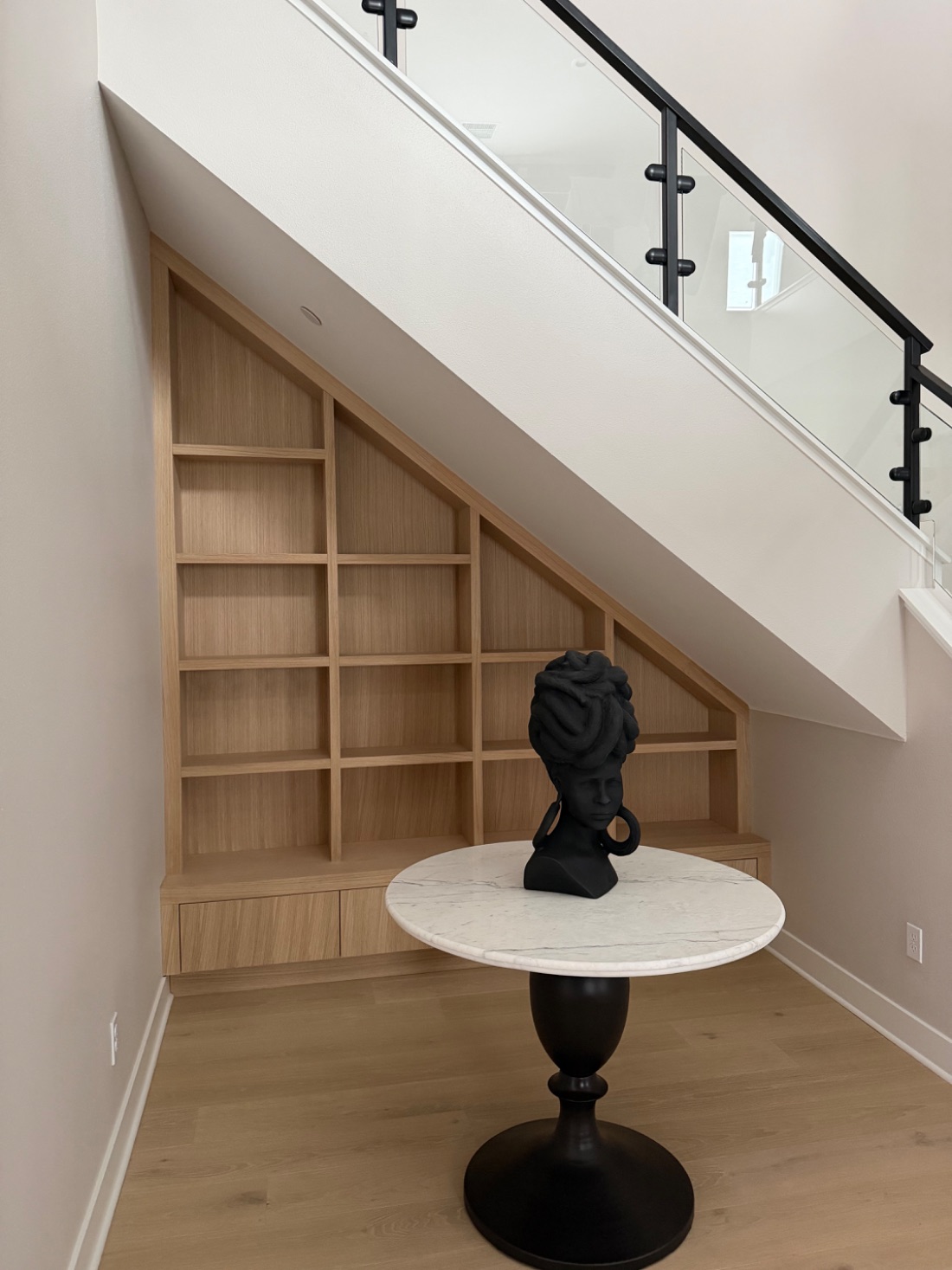 A custom white oak bookcase fitted beneath a staircase, with angled shelves following the slope.